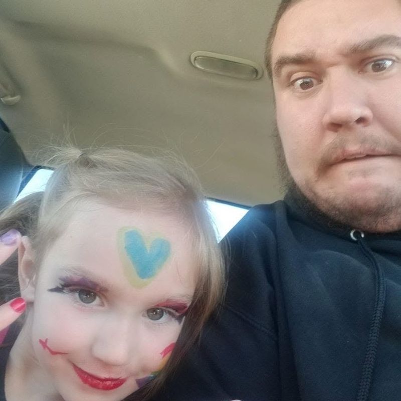 Layton and his daughter smiling in the car, her face painted with a blue heart.