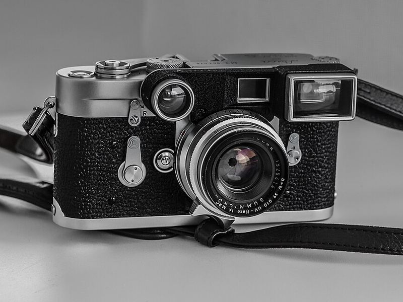 A rangefinder film camera with a strap, in black and white