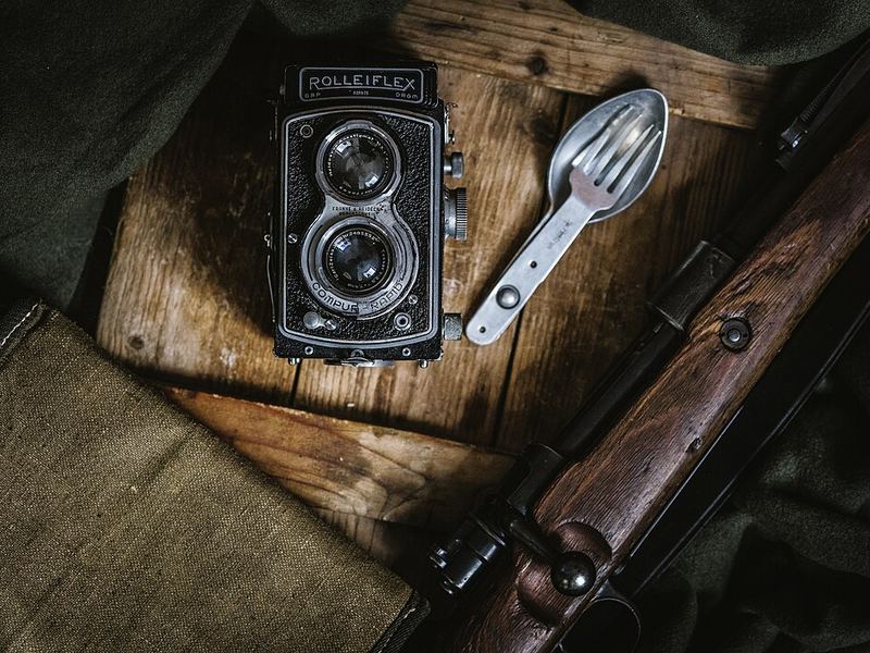 A twin-lens reflex camera next to a folding spoon on a wooden crate