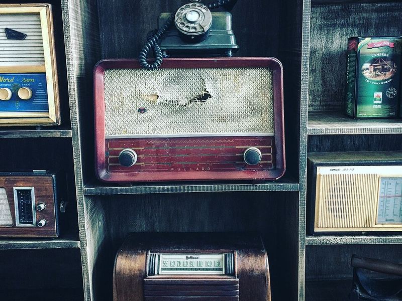 A collection of old tube radios and a rotary phone on wooden shelves