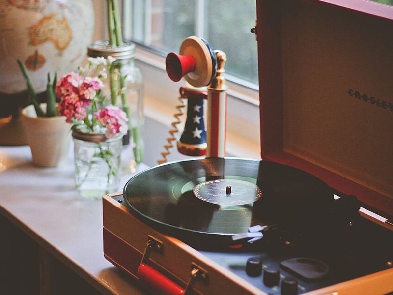 A record player in an orange case on a windowsill beside flowers and an old telephone