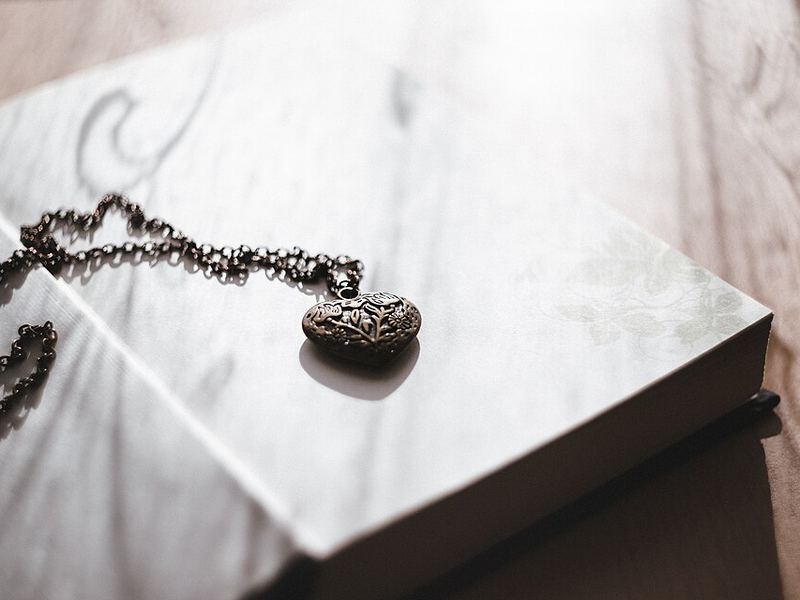 A silver locket on a chain resting on an open book