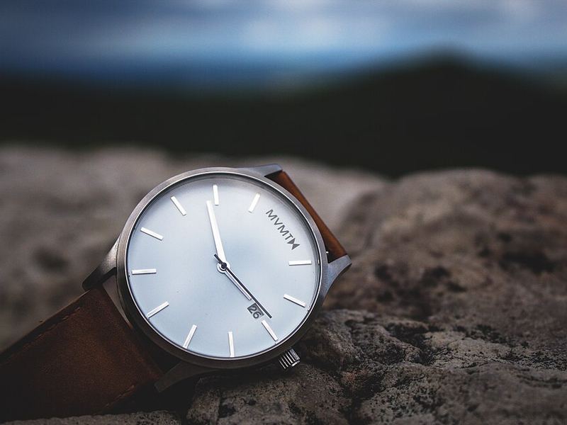 A wristwatch with a white face and brown leather strap on a rock