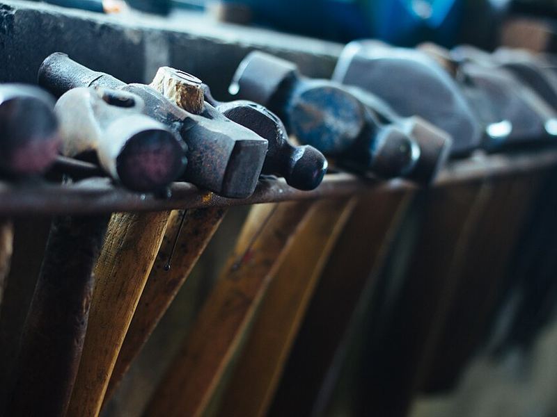 A row of old hammers with worn wooden handles