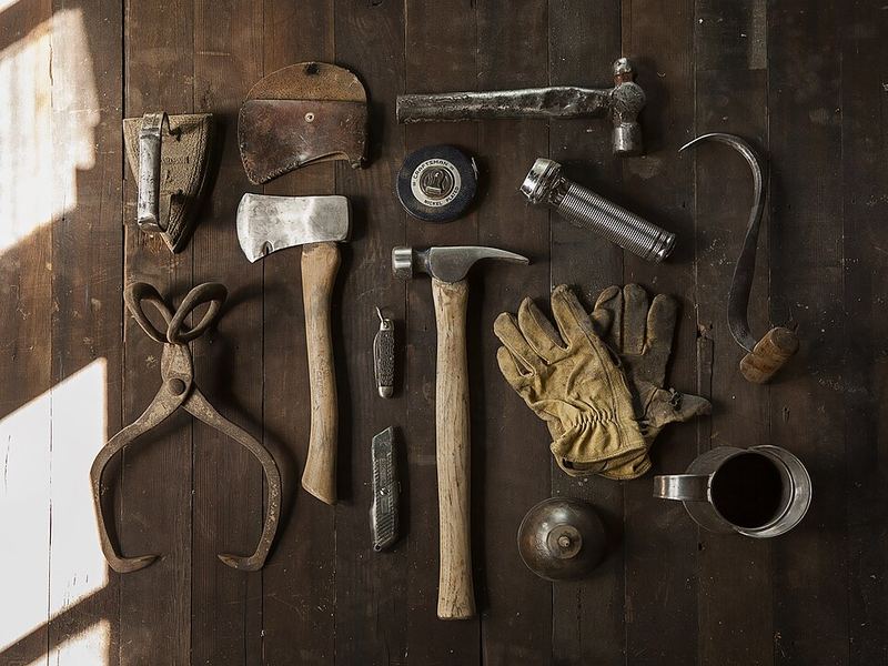 Old hand tools, work gloves and an axe laid out on wooden boards