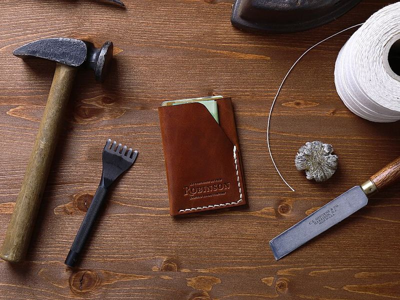 A hammer, a leather wallet, a knife and a spool of twine on a wooden table