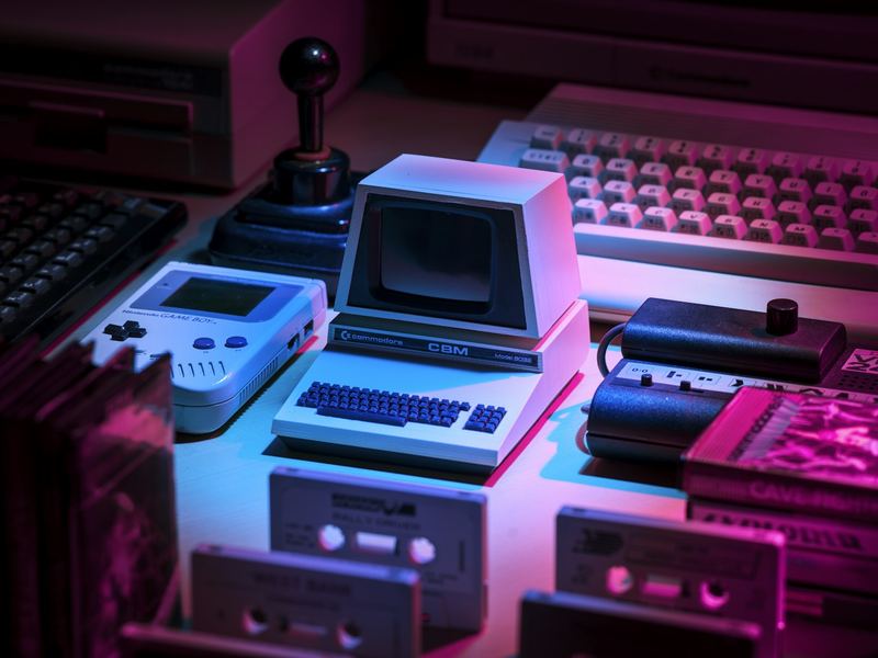 Vintage game consoles, a joystick and cartridges under pink and blue light