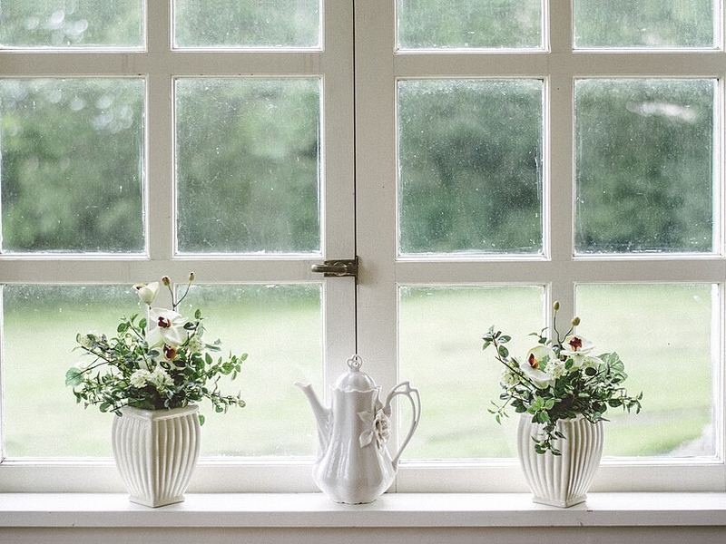 A white porcelain teapot between two potted flowers on a sunny windowsill