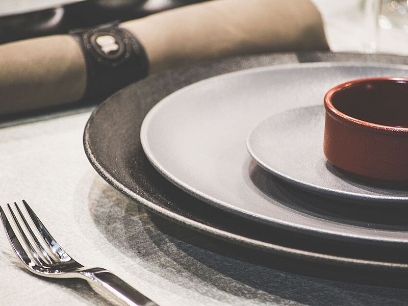 Gray stoneware plates stacked with a small red bowl, a fork and a linen napkin