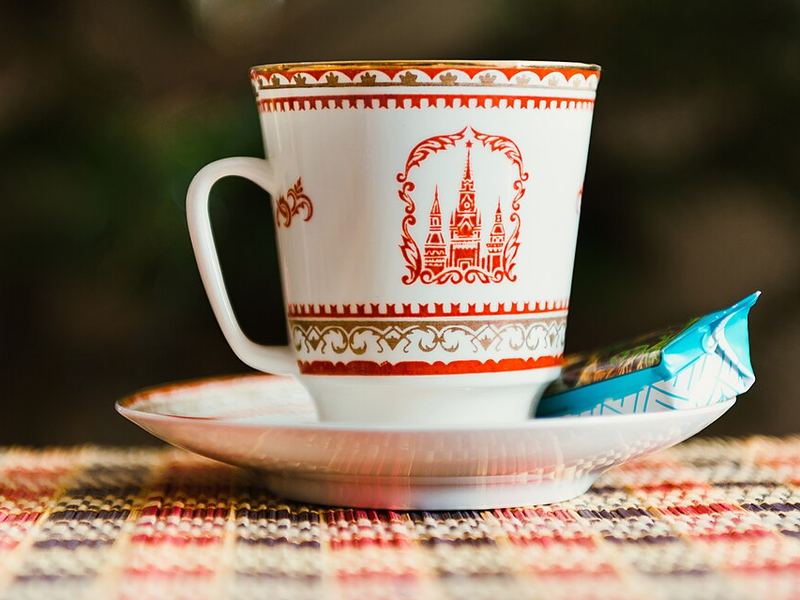 A porcelain cup with a red Kremlin pattern on its saucer, with a wrapped candy