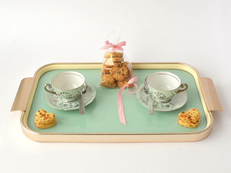 Two floral teacups on saucers on a mint-green serving tray with cookies