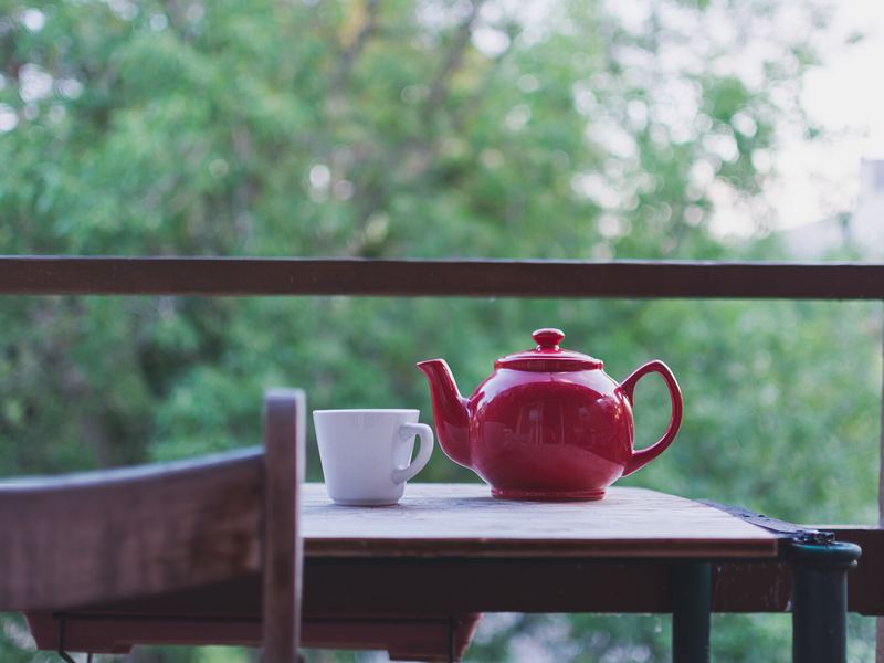 A red teapot and a white cup on a small table on a balcony